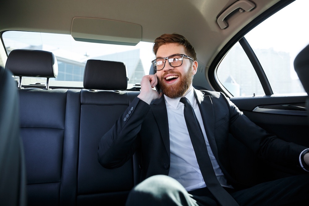 Business traveller taking a call in the back seat of a London airport taxi transfer while the driver handles the route to the terminal
