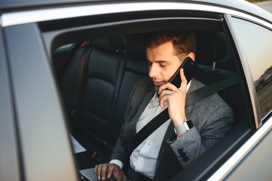 Business traveller working on a laptop and taking a call in the back seat of a taxi to Luton Airport